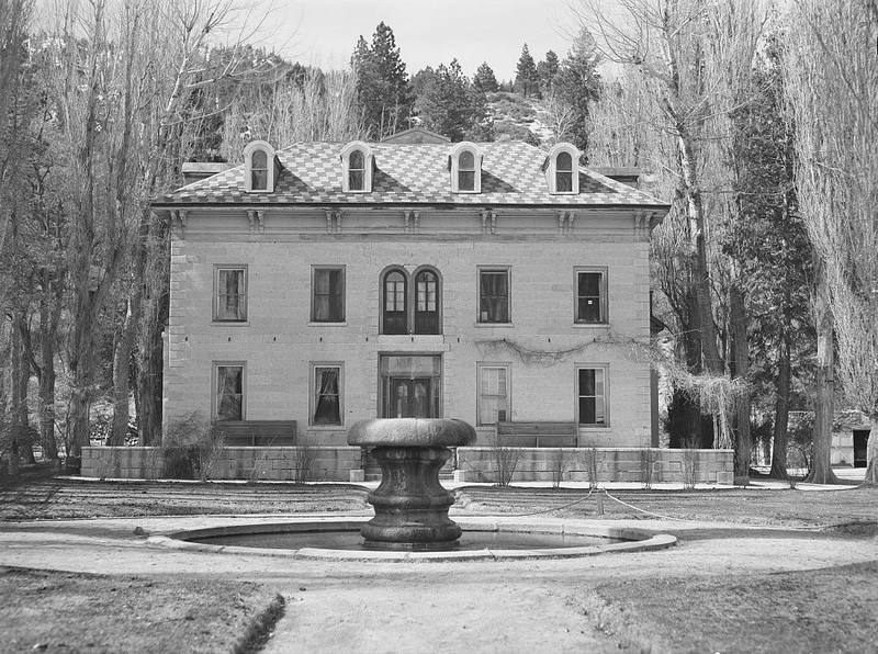 The Bowers Mansion in 1940, long after Eilley's time: a two-storey stone house with a patterned roof and dormer windows, a round fountain in front and bare trees around it. Black-and-white photograph.